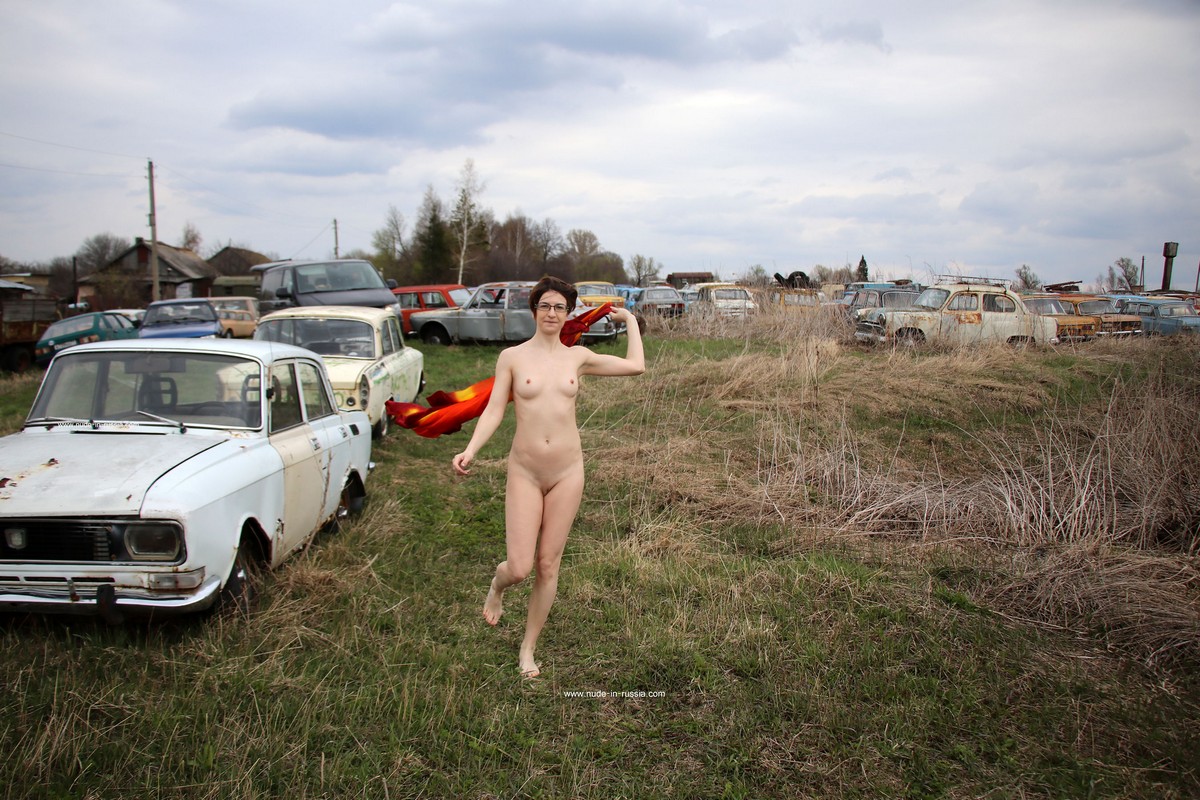 A short-haired naked girl Atisha walks through the museum of old Soviet cars