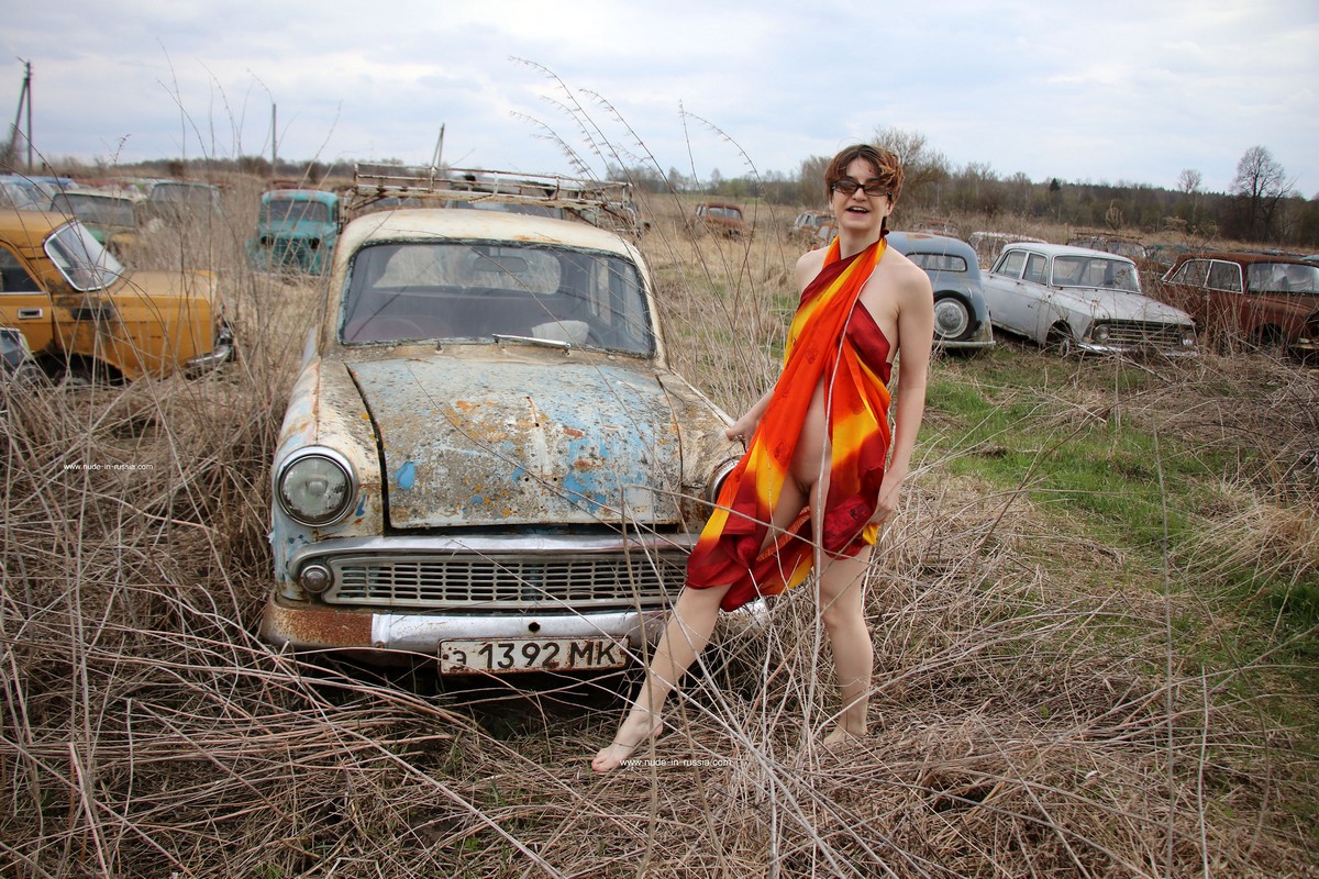 A short-haired naked girl Atisha walks through the museum of old Soviet cars