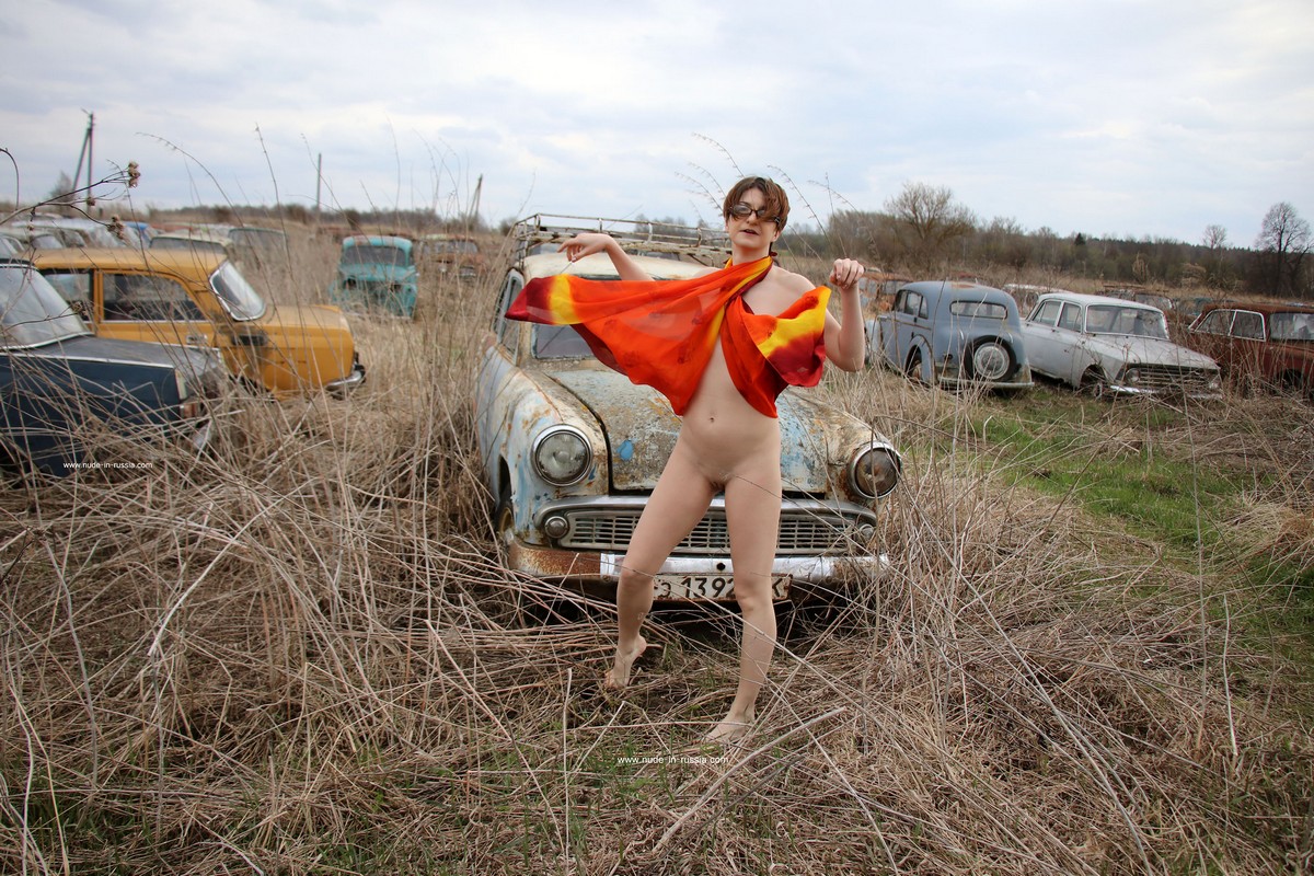 A short-haired naked girl Atisha walks through the museum of old Soviet cars