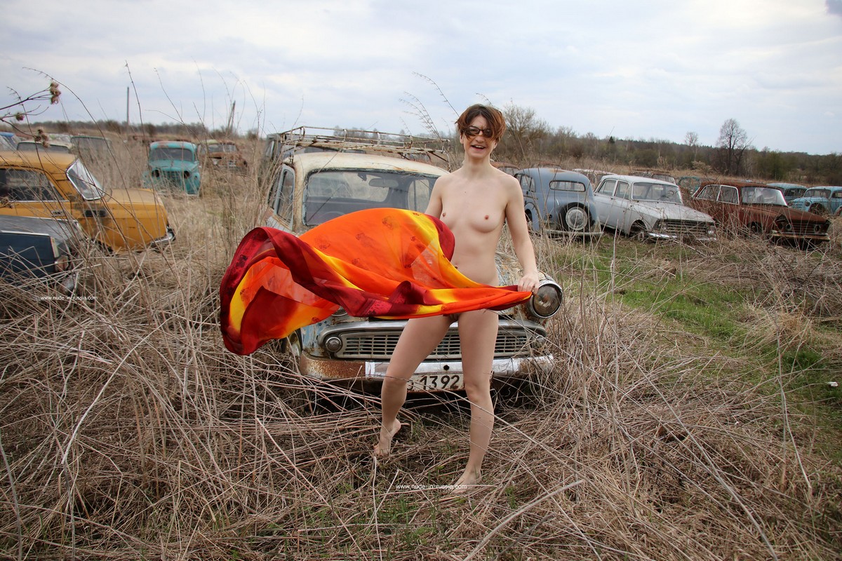 A short-haired naked girl Atisha walks through the museum of old Soviet cars