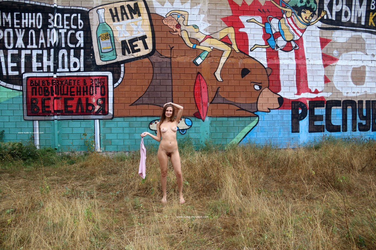 A cute Russian girl with a hairy pussy takes a photo in front of a colorful mural