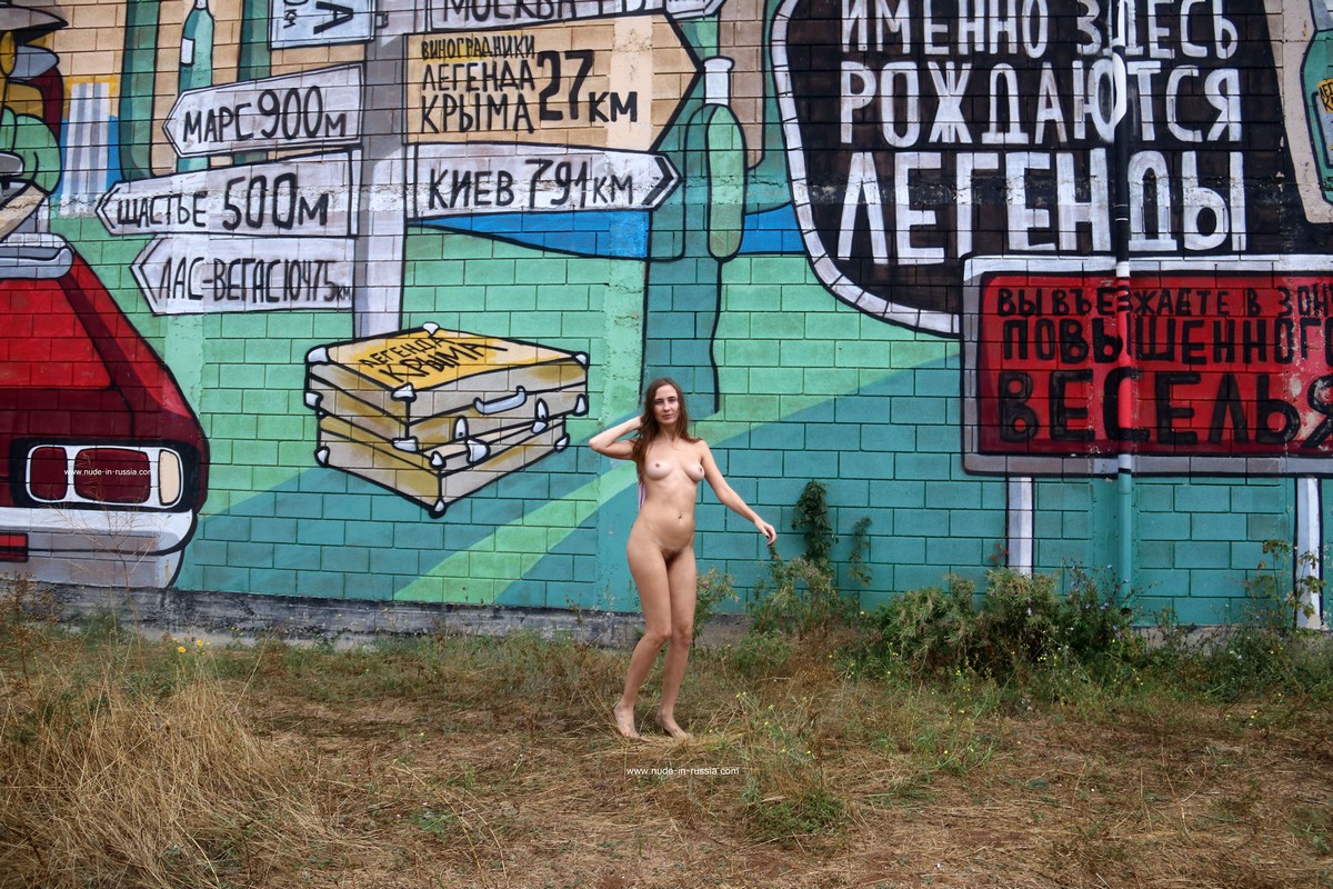 A cute Russian girl with a hairy pussy takes a photo in front of a colorful mural
