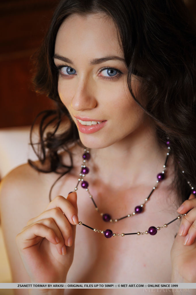 Dark, curly hair frames Zsanett Tormay's beautiful face, her sparkling blue eyes stare seductively towards the camera as she sprawls naked on top of the bed.